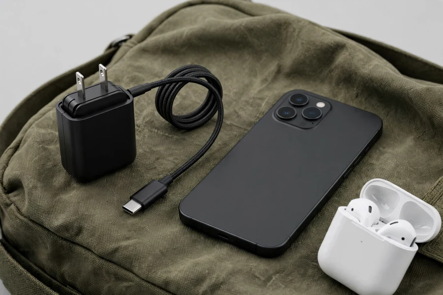 Tiny black USB-C wall charger with retractable cable beside a phone on a travel bag